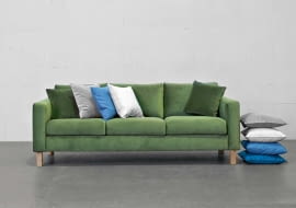 Sofa Kera to połączenie prostej formy i wygody. Występuje w różnych rozmiarach i obiciach, m.in. w aksamitnej tkaninie o głębokim odcieniu zieleni.