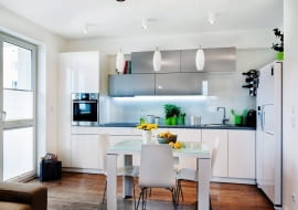 PRZECHOWYWANIE W KUCHNI. System trójkowy. Stół, stanowiący umowną granicę między strefami o różnej funkcji, oświetlają trzy lampy z podłużnymi kloszami, natomiast część kuchenną - oprawy sufitowe Massive Pillar. Pod górnymi szafkami dodatkowo zamontowano halogeny, których światło pada bezpośrednio na blat roboczy.