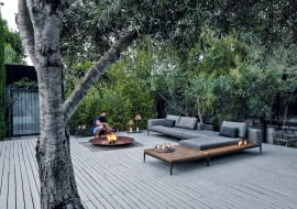 Wokół ognia. Prawda, że te rozłożyste kanapy marki Gloster wyglądają jak wystawione na taras z salonu? I o to właśnie chodzi! Grid to rozbudowany system modułowych mebli tarasowych. Miękkie siedziska i postumenty wykończone w teakowym drewnie pozwalają na komponowanie tarasowej przestrzeni w dowolny sposób. gloster.com