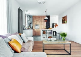 W SZAROŚCIACH I BRĄZACH. Niebanalny stolik z blatem zdobionym motywem mandali gospodyni zamówiła w sklepie guido.pl. Zabudowa kuchenna, zrobiona ze szczotkowanego dębu, mieści lodówkę oraz szafki (wśród nich cargo). Na podłodze w pokoju dziennym leżą dębowe deski, natomiast w kuchni - wzorzyste płytki marki Vives oraz beton firmy Mercadier. Duży grzejnik na ścianie to model Charleston firmy Zehnder.