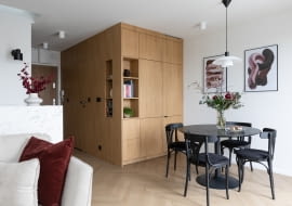 Ściana i zabudowa meblowa we wspólnym wykończeniu drewnem tworzą atrakcyjną, zwartą, architektoniczną formę – swego rodzaju kubik. Skrywa on łazienkę, lodówkę oraz szafę do przechowywania.