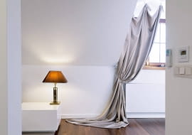 <B>Nocą do tej sypialni zaglądają tylko gwiazdy, nie ma więc potrzeby szczelnego zasłaniania małych okien. Wiszące tu zasłony mają inne zadanie - zdobienie wnętrza. I wywiązują się z niego znakomicie.</B> </BR> Do udrapowanej na stałe tkaniny, ścielącej się po podłodze, doszyto troczki z haczykami, które zaczepia się na gałkach przymocowanych do  ściany nad oknem. Takich samych gałek użyto do podpięcia zasłon. Taka aranżacja wygląda nieco teatralnie, ale efektownie.