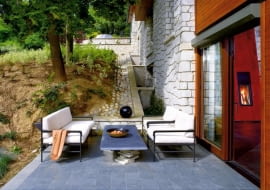 W tym domu dopilnowano, by posadzka wewnątrz i na tarasie była na tym samym poziomie. Wyściełane, wygodne meble nawiązują do tych z wnętrza. Taras osłania skarpa, w którą wkomponowano budynek