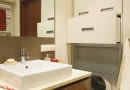 Pralkę przesłaniają drzwi z aluminiowych żaluzji. Nad nią we wnęce znajdują się szuflady i szafka z płyty MDF zamykana drzwiczkami.