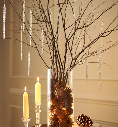 Nagie gałęzie drzew zimą często pokrywają się szadzią i lodem. Ten sam klimat można stworzyć w domu, w szklanym wazonie. Wystarczy wstawić do niego sznur lampek (najlepiej diodowych), szyszki i gałęzie brzozy. Do tego akrylowe sople... I dekoracja gotowa. www.blog.1800flowers.com