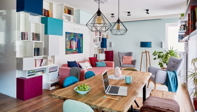 Do kolorystyki regału z pojemnymi schowkami i otwartymi półkami nawiązują odcienie poduszek. Na półkach jest jeszcze trochę wolnego miejsca na książki. Za listwą pod sufitem znajduje się rozwijany ekran - Justyna ogląda na nim filmy z rzutnika zamontowanego na środku sufitu.