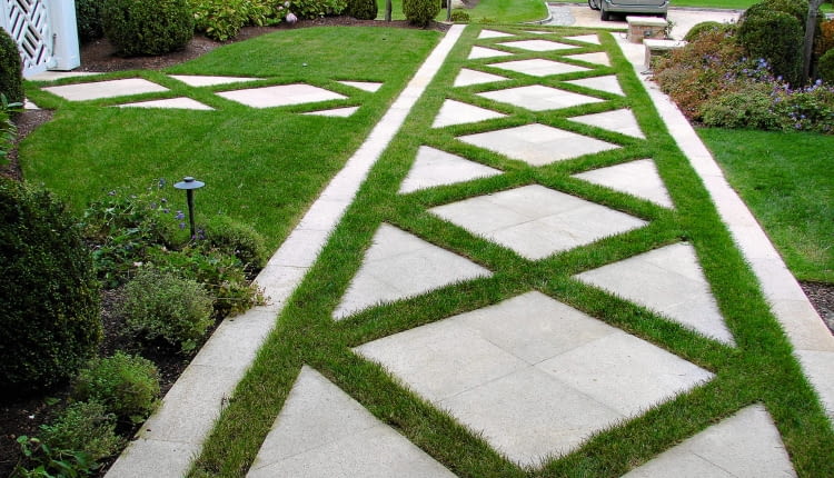 W KRATKĘ Aby uzyskać taki efekt, na betonowej podbudowie wzmocnionej siatką zbrojeniową układamy duże płyty, pozostawiając między nimi przerwy wypełnione ziemią kompostową (w której wysiewamy trawę). Płyty przyklejamy do podbudowy mrozoodporną zaprawą klejową. Najlepsze są płyty z warstwą wykończeniową typu terrazzo (ze wzmocnionym betonem od spodu, a polerowaną warstwą cementu i kruszywa od góry), z powierzchnią zabezpieczoną przed poślizgiem (płomieniowaną, żłobkowaną lub matowaną).