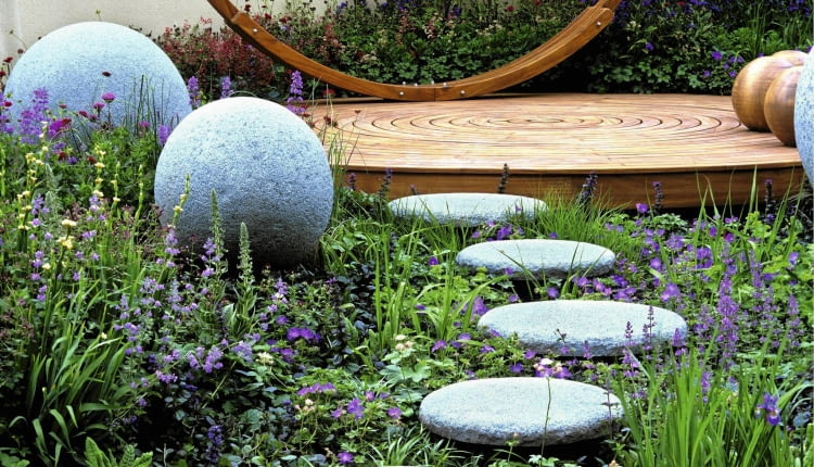 Modern outdoor room has unifying theme of circles and spheres.Concrete balls and stones lead to deck and hammock. Blue ajuga, nepeta and geranium SLOWA KLUCZOWE: Designer Garten Hof Holz H ngematte Kreis Kreise Pflanze Stein Storchschnabel Storchschn bel Trittsteine Wege ausspannen bl´hend enspannen entspannend entspannt erholend friedlich friedvoll geschwungen kreisf^rmig krumm modern relaxed relaxen ruhen zeitgen^ssisch Nicola Stocken Tomkins quadratisch
