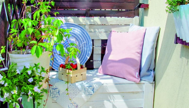 Oparcie balkonowej ławy zostało namalowane na drewnianym ekranie. Na pierwszym planie pomalowany na niebiesko wiekowy kociołek w roli donicy.