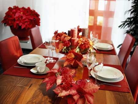 Nastrojowa dekoracja stołu. Poinsecje ułożono w niskich naczyniach z pojedynczymi goździkami i nerine.