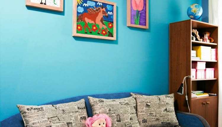 METAMORFOZY POKOJU DZIECKA. Starą sofę zastąpiono nową, większą. Mebel w zgaszonym odcieniu niebieskiego i chłodnej szarości ożywiły poduchy w modny gazetowy wzór. Tkaniny zostały wybrane z próbnika przez Maję i rodziców. Łóżko wygląda więc tak, jak chciała dziewczynka. Na jasnoturkusowej ścianie - wystawa prac Mai.