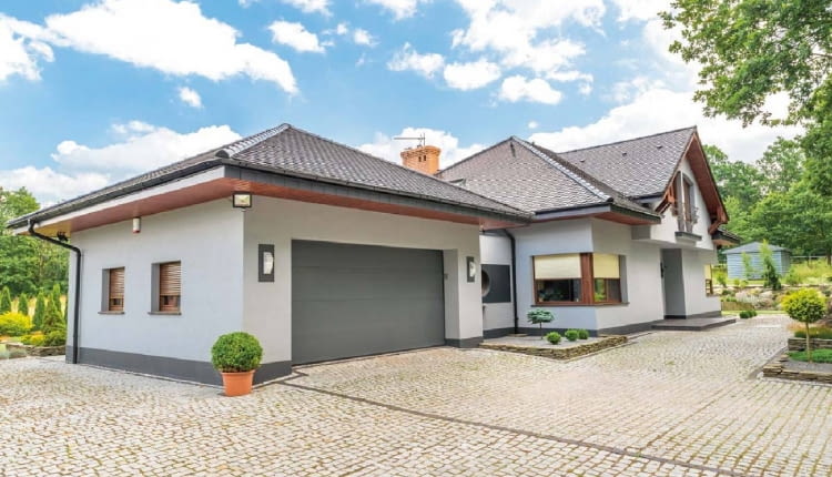 Grafitowa brama garażowa - taki sam kolor ma cokół i pas na tynku łącznika między domem a garażem