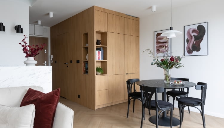 Ściana i zabudowa meblowa we wspólnym wykończeniu drewnem tworzą atrakcyjną, zwartą, architektoniczną formę – swego rodzaju kubik. Skrywa on łazienkę, lodówkę oraz szafę do przechowywania.