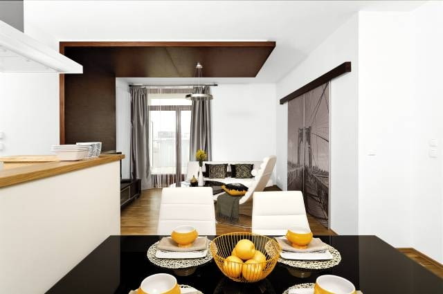 Bez kolorystycznego szaleństwa - jasny brąz dębowej podłogi i biel tapicerowanych mebli obitych skórą ożywiają jedynie żółte dodatki. Szare zasłony w oknie harmonizują z czarno-białą fotografią na drzwiach.