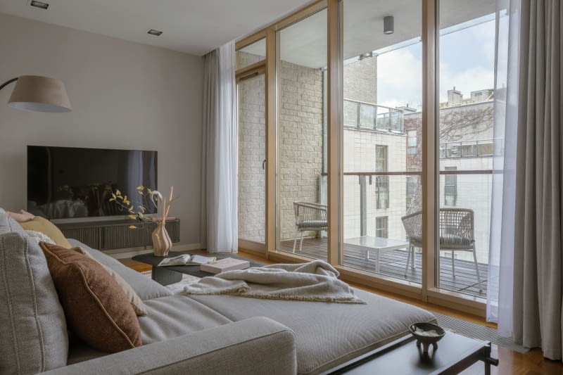 Salon otwierający się na loggię poprzez panoramiczne przeszklenie  to wymarzone miejsce  do przesiadywania i podpatrywania miejskich widoków.