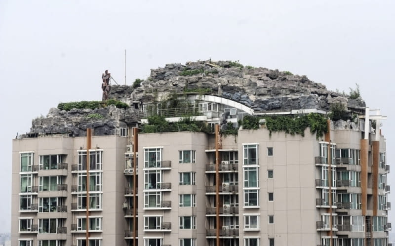Dwupiętrowa rezydencja na szczycie 26-piętrowego wieżowca. This Aug. 12, 2013 photo released by Chinas Xinhua News Agency shows a residential building with a rocky style villa on its roof, in Haidian District of Beijing, China. Beijing authorities are planning to demolish the bizarre rooftop villa embedded in rocks, trees and bushes that allegedly was built illegally atop a 26-story apartment block in the capital. (AP Photo/Xinhua, Luo Xiaoguang) NO SALES