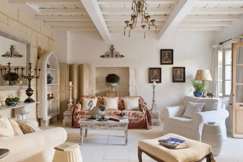 Stone floored provencal sitting room with armchairs, floral sofa throw and distressed wooden coffee table SLOWA KLUCZOWE: provence france french provencal inside indoors day nobody interior design home living room drawing room sitting room sofa floral pattern cream colour artwork seating area animal likeness swan bird shelves shelving tiled floor painted furniture shabby chic white white colour armchair country style horizontal image colour image