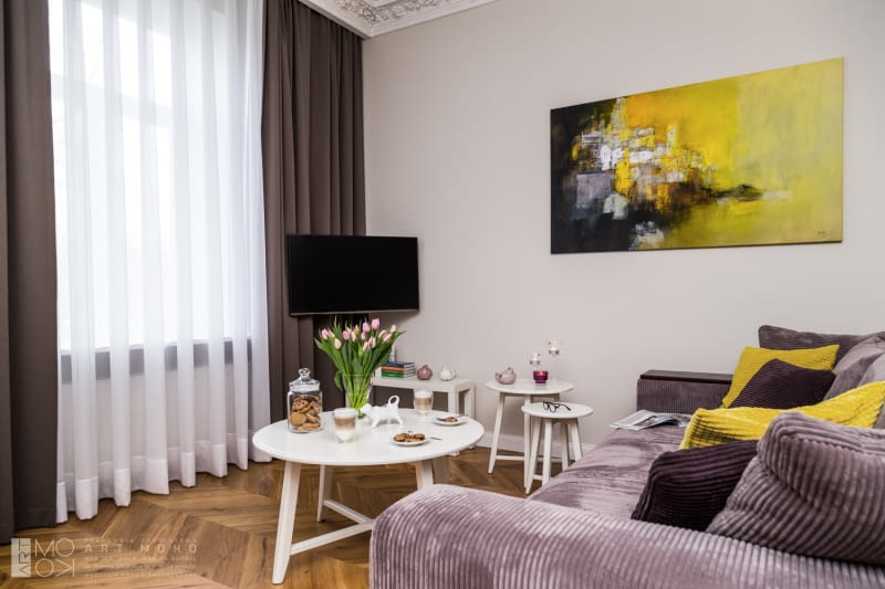 Po przeciwnej stronie kącika jadalnego zaaranżowano salon - na zasadzie przeciwwagi urządzono go w nowoczesnym klimacie. Rozkładana sofa i poręczne stoliki kawowe tworzą wygodną strefę wypoczynku. Tu również znalazło się miejsce dla sztuki - na ścianie pejzaż Rogera Lane. aranżacje wnętrz, zdjęcia mieszkań, mieszkanie w Krakowie