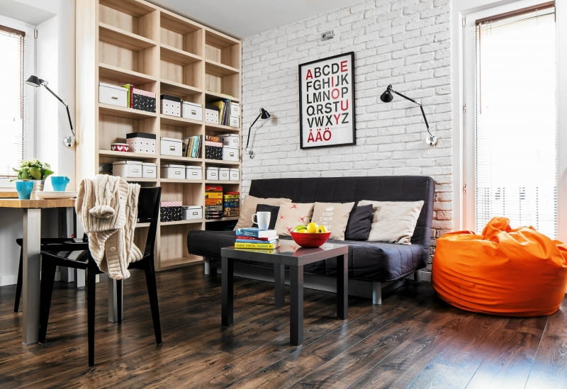 Funkcjonalnie i stylowo. Lekka kanapa z funkcją spania nie zajmuje dużo przestrzeni. Drewniany regał na całą ścianę zapewnia miejsce na przechowywanie. mały salon w bloku, aranżacje