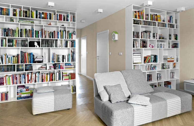 Dwa duże regały, zrobione na wymiar z malowanej płyty MDF, mieszczą domową biblioteczkę. Dwukolorowe, biało-szare meble wypoczynkowe (z firmy Agata) zdradzają zamiłowanie gospodarzy do spokojnych barw. salon, aranżacja salonu