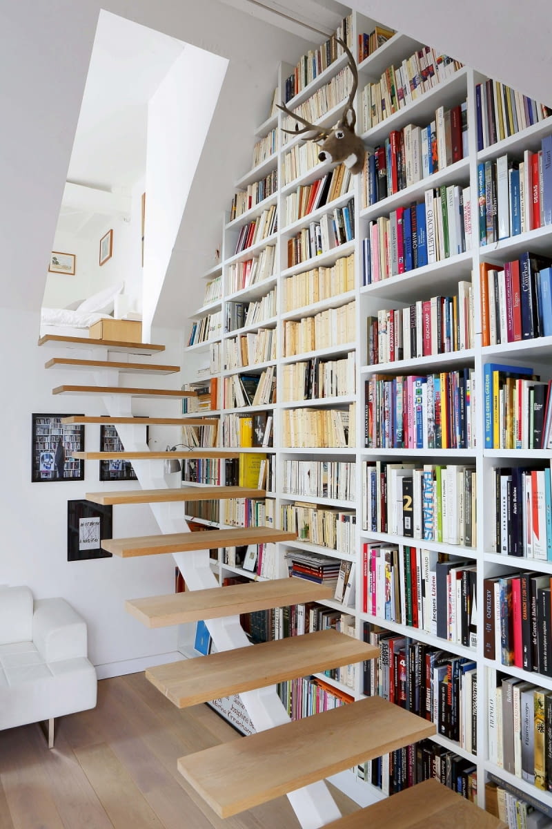 POD SKOSEM. Bardzo pojemna biblioteczka została ulokowana przy schodach prowadzących na antresolę. Półki zaprojektowano pod wymiar książek. Półki na książki warto zaprojektować pod swoje zbiory. Jeśli mamy dużo albumów - część z półek powinna być wyższa i głębsza niż standardowe. Najmniej będą przeszkadzały, jeśli umieścimy je na samej górze biblioteczki. OSous et sur les toits, larchitecte Philippe Chiambaretta et sa femme leditrice Julie Rouart rcgnent au sommet dune joyeuse tribu. Dans cet espace retranche, cerne de verdure, lart, les livres et les lignes campent une humeur dilettante o? pavoise le go?t de la creation.--Gros plan sur limmense bibliothcque montant jusquau toit.