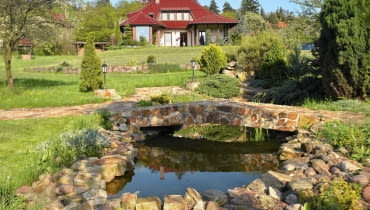 Malownicza willa przytulona do wzgórza ma za tło skarpę porośniętą gęstwiną drzew i krzewów.