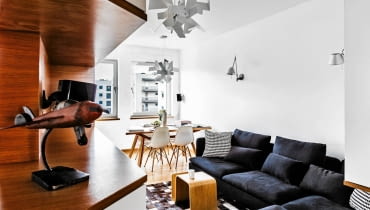 <B>Aleksander, prawnik z zawodu, a z zamiłowania pilot awionetki, chciał, by jego pasja znalazła wyraz w wystroju wnętrz. Patrząc na meble i dodatki nawiązujące do formy samolotu, nie ma wątpliwości, że projektantom udało się sprostać temu niecodziennemu wyzwaniu.</B> <BR />Pokój dzienny, tak jak i całe mieszkanie, został zaaranżowany minimalistycznie, ale nie bezosobowo, co w tym stylu często się zdarza. Dzięki&#8200;elementom wystroju nawiązującym do&#8200;lotniczej pasji gospodarza wnętrze nabrało osobistego charakteru.