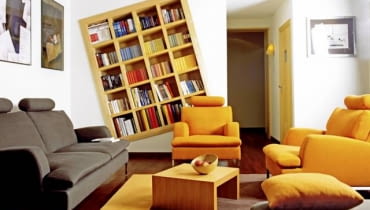 Na przekór. Jak mówią gospodarze tego mieszkania, pokój dzienny, w którym znajduje się domowy księgozbiór, miał być zaaranżowany "nie do końca na serio, z lekką nutką designerskiej przekory". Trzeba przyznać, że ten zamysł udało im się zrealizować w stu procentach. Niekonwencjonalny regał na książki - regularna, modułowa konstrukcja z drewna, wbudowana skosem w ścienną wnękę - może przyprawić o prawdziwy zawrót głowy! WNETRZA MEBLE