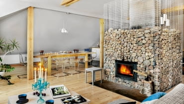 Kamienie w okalającym kominek gabionie to nie tylko efektowna dekoracja. Gdy płonie ogień, szybko się nagrzewają, a potem oddają ciepło jeszcze długo po wygaśnięciu paleniska mieszkanie, wystrój wnętrz, kominek, salon z kominkiem