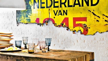 Ceglana ściana pomalowana na biało nie przytłacza wnętrza. Stół na metalowej konstrukcji, z grubym drewnianym blatem (tutaj z desek położonych na sztorc) to mebel prawie obowiązkowy. Do kompletu proste talerze z drewna mango, 36 zł/szt., Square Space styl loftowy, wnętrza loftowe, ceglana ściana, stół na metalowej konstrukcji, Square Space