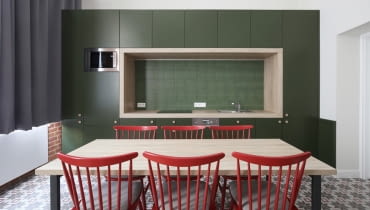 Na aranżację kuchni świetnie wpływa kontrast między zieloną zabudową, a czerwonymi krzesłami. Oryginalne mieszkanie w Krakowie