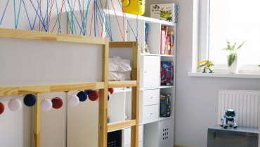 PO ZMIANIE. Pojemny re-gał ułatwił zaprowadzenie porządku wśród zabawek i gier. Sporo rzeczy mieści się też w metalowej skrzyni, która służy również jako siedzisko. Część drewnianych skrzynek po zawieszeniu na ścianie zamieniła się w dodatkowe półki. pokój dziecięcy, meble dziecięce, metamorfoza wnętrz