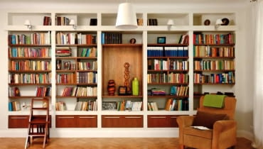 Regał z płyt gipsowo-kartonowych zajmuje całą szerszą ścianę pokoju-biblioteki. Drewniane schodki umożliwiają sięganie po książki z wyższych półek. Wnętrze wydaje się jeszcze większe, niż jest w rzeczywistości. To dzięki jasnej kolorystyce z dominującą bielą w dwóch odcieniach (śnieżnym oraz kremowym), przełamaną barwą podłogi, półek i fotela. regały na książki