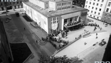 Kino wybudowano w latach 1956 - 1960 na tyłach Nowego Światu w Warszawie. Zachwycał modernistyczną bryłą, a także malarstwem i ceramicznymi zdobieniami we wnętrzach. Widzów zapraszał modny neon. Dziś w miejscu zburzonego budynku stoi pięciopiętrowy apartamentowiec. Na zdjęciu ludzie stojący w kolejce do kasy. Widoczne dekoracje reklamujące film "Krzyżacy", którego premiera miała miejsce w 1960 roku. Kino Skarpa w Warszawie - Ludzie stojący w kolejce do kasy. Widoczne dekoracje reklamujące film "Krzyżacy".