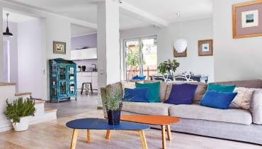 PRZESTRZEŃ I ŚWIATŁO - w tym domu z pewnością ich nie brakuje. Kąt wypoczynkowy od kuchni i jadalni wizualnie oddziela podłoga: w salonie położono bielony dąb szczotkowany, w pozostałej części gres. Szarą kanapę, stoliki kawowe Melisa w odcieniach dżinsu i brandy, zielone i granatowe poduszki oraz osłonki na do- niczki z trawą i rozmarynem kupiono w sklepie Nap.