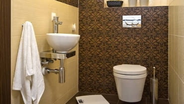 Układ idealny. Brązy, beże i dekoracyjne płytki z motywem liści, które podkreślają kształt wnęki nad podwieszanym sedesem. Układ idealny. Brązy, beże i dekoracyjne płytki z motywem liści, które podkreślają kształt wnęki nad podwieszanym sedesem.