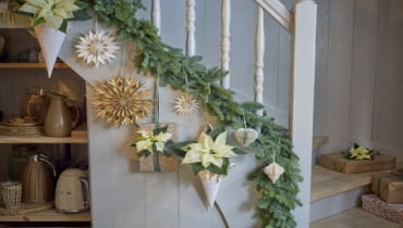 Kremowo-białe poinsecje, zarówno cięte, jak i doniczkowe, zdobią balustradę i prezenty.