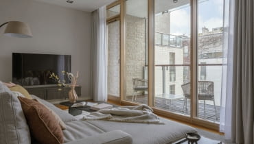 Salon otwierający się na loggię poprzez panoramiczne przeszklenie  to wymarzone miejsce  do przesiadywania i podpatrywania miejskich widoków.