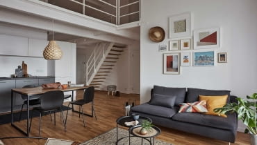 Wyposażenie apartamentu łączy urok prostych, nowoczesnych elementów wykończenia z tymi nawiązującymi do trendu etno. Plecione kosze, ręcznie tkane dywaniki to dodatki pojawiające się w całym mieszkaniu. salon z aneksem kuchennym