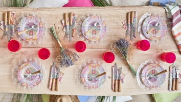 Surowy, drewniany stół, kolorowe talerze i kwiaty. Takie nakrycie stołu to esencja lata. nakrycie stołu, przyjęcie