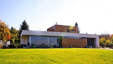 Dom wybudowany według projektu gotowego pracowni Archon+ wygląda trochę jak łódź podwodna wynurzająca się z morza trawy nowoczesny dom