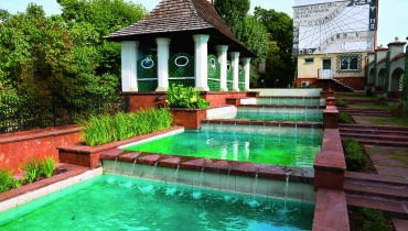 Kaskada wodna , a ltana i zegar słoneczny na ścianie budynku, z mottem Wincentego Kadłubka: "Lepiej stracić rzeczy niż czas".