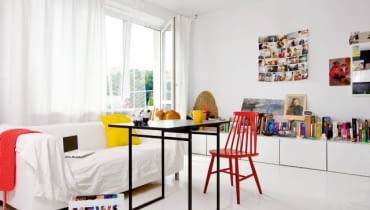 Wszechobecna biel powiększa optycznie małe mieszkanie (38 m kw.). Blaty szafek (takie same wiszą w kuchni) pełnią funkcję biblioteczki i miejsca na bibeloty i zdjęcia. Na podłodze - malowane deski. Kotka Sissy, trzeci domownik, puszy się na oparciu kanapy.