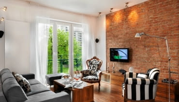 Stonowana kolorystyka (tylko brąz, czerń i szarość na tle białych ścian i zasłon) oraz niewielka liczba sprzętów podkreślają przestronność wnętrza. Nowoczesna kanapa i puf, obite alcantarą, zyskały bardziej szacowne towarzystwo - fotele z targu staroci, którym po wymianie zniszczonych obić przywrócono dawną urodę. salon, ceglana ściana, aranżacje wnętrz