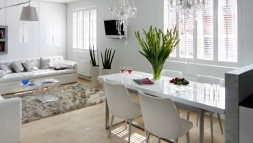 Wyspa - główne miejsce pracy - została przesłonięta nieco od niej wyższym murkiem. Ponieważ nie zasłonił on całkowicie mebli kuchennych i wysokiej zabudowy, wybrano szafki z frontami w kolorze ściany, co wtopiło je w tło. Aby nic nie rozbijało ich gładkiej płaszczyzny, zdecydowano się na szafki otwierane dotykowo. Harmonię we wnętrzu podkreślają użyte materiały wykończeniowe - na podłodze, tak jak w pozostałej części pomieszczenia, leżą panele, a ścianę we wnęce nad zlewem pokryto dekoracyjnym tynkiem strukturalnym. Przy murku od strony salonu znajduje się część jadalna. Blat sporego stołu jest zrobiony z takiego samego materiału co fronty szafek - płyty lakierowanej na wysoki połysk.