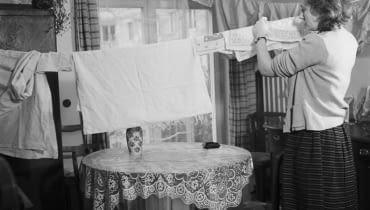 Polskie mieszkania w ciągu ostatnich 100 lat przeszły diametralne przemiany. W dwudziestoleciu międzywojennym wnętrza urządzane były z dużą starannością, meble i dodatki wybierano na lata, tak by służyły kilku pokoleniom. Nie było więc mowy o prowizorce. Ściany obficie zdobiono obrazami, grafikami, tkaninami, a czasem mapami i różnego rodzaju trofeami. Druga wojna światowa, a następnie niesprzyjający ustrój spowodowały, że naturalny rozwój stylu został na długo zahamowany. W mieszkankach Polaków zagościły dokładnie takie same meble i dekoracje. Meblościanki, tapczany, wersalki, boazerie, ale też polska ceramika były powtarzalnymi elementami w niemal każdym wnętrzu. Zmiana ustrojowa w 1989 roku otworzyła drzwi na nowe i przyniosła zachwyt zachodnimi wzorcami oraz nieposkromioną wolność w kreowaniu przestrzeni prywatnych. Dziś wciąż pozostajemy pod silnym wpływem zagranicznych stylów, jednak podchodzimy do nich bardziej krytycznie niż to miało miejsce jeszcze 10-15 lat temu. Obecnie typowe polskie mieszkanie to coraz częściej pokój połączony z kuchnią, współczesna wersja meblościanki z telewizorem w centralnej części i obowiązkowo jakiś mebel z IKEA. Jest to obraz zgoła odmienny od tego, co było w latach 20 i 30. </BR></BR> <B>Ok. 1955 r.: Kobieta rozwieszająca na sznurku w pokoju wypraną bieliznę.</B> polskie wnętrza, jak mieszkają Polacy