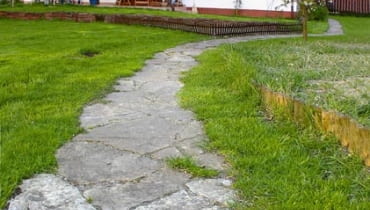 Ścieżka z łamanych płyt kamiennych. Przestrzenie między poszczególnymi płytami są zasypane piaskiem i zarośnięte kępkami traw. DO JEDNORAZOWEJ PUBLIKACJI