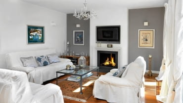 Wokół kominka (i zamontowanego nad nim telewizora) skupia się domowe życie. Zanim kominek został zbudowany, projektantka zrobiła jego tekturową makietę w skali 1:1, żeby sprawdzić, czy proporcje są odpowiednie. Po lewej obraz Stasysa Eidrigeviciusa, po prawej baletnica Bereniki Koreckiej; nad kanapą płótno Alicji Słaboń-Urbaniak. Drewniany świecznik stojący na podłodze to nabytek z paryskiego targu staroci, latarenka na stoliku - ze sklepu BBHome. Salon z kominkiem, kominek, wystrój salonu