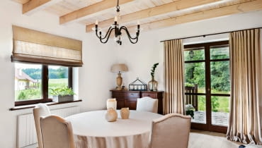 <B>Wnętrze zostało urządzone w rustykalnym stylu, dlatego pani domu udekorowała okna prosto drapowanymi zasłonami z lnianego płótna. Aranżacja jest równie naturalna i piękna jak Puszcza Knyszyńska widoczna na horyzoncie.</B> <BR />Długie zasłony w drzwiach balkonowych i rolety w oknie uszyto z grubego, gęsto tkanego lnu. Pani domu tak podoba się ten rodzaj tkaniny, że wybrała ją także na obicia krzeseł, obrus oraz abażur lampy.