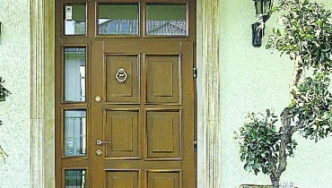 Jasna kolorystyka elewacji to również jasne drzwi. Ich urodę podkreśla ozdobne obramowanie drzwi i przeszklona ścianka.